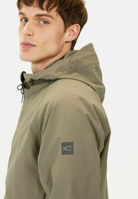 Kapuzenshirt in olivgrün, mit strukturiertem Stoff, verstellbarem Kordelzug und einem Logo-Patch auf dem linken Ärmel.