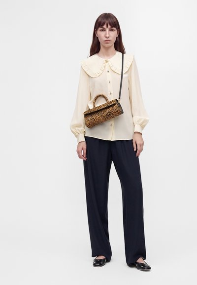 Femme portant un chemisier crème avec un grand col, un pantalon noir à jambes larges, des ballerines noires et un sac à main à imprimé léopard avec une bandoulière.