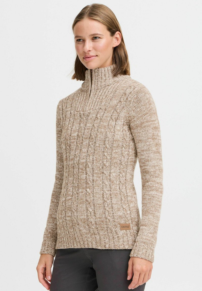 Beige kabelstrickpullover mit hohem Kragen und gerippten Bündchen; verfügt über ein strukturiertes Muster und ein dezentes Logo-Tag am Saum.