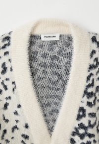 Mjukt och fluffigt cardigan med svart och grå leopardmönster samt kr�ämfärgad sjalkrage, visar "YOURTURN" märklapp.