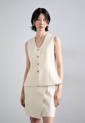 Beige tailored vest with a v-neckline and five gold buttons, paired with a matching knee-length skirt featuring a diagonal cut.