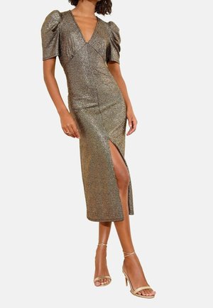 Mujer que lleva un vestido midi dorado brillante con mangas cortas abullonadas y una abertura hasta el muslo, combinada con sandalias doradas de tacón alto con tiras.