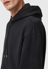 Czarny hoodie o luźnym kroju, wykonany z teksturowanej tkaniny, z kapturem na sznurku i minimalnymi detalami szwalniczymi.