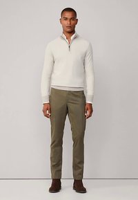 Lichtgrijze gebreide herentrui met ritssluiting, gecombineerd met olijfgroene slim-fit broek en bruine enkellaarzen. Eenvoudig, modern ontwerp.