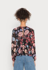 Blusa preta floral com mangas longas e bufantes, apresentando um padrão floral em rosa e azul. Inclui uma abertura em forma de gota nas costas e uma bainha peplum.