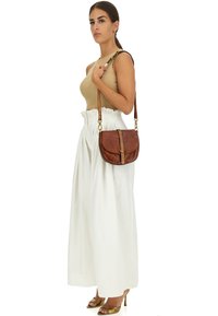 Borsa a tracolla in pelle marrone con forma curvata, dettagli in metallo dorato e finitura texturizzata, indossata su uno sfondo bianco.