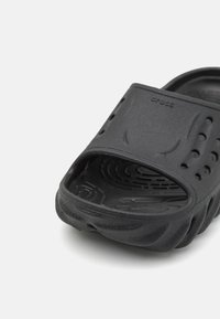 Černé skluzové sandály vyrobené ze syntetického materiálu, s ventilačními otvory, texturovanou podrážkou a zakřiveným designem pro pohodlí.