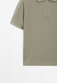 Khaki polo triko s krátkým rukávem, poloviční zip, ribované textury a rovný lem. Jednoduchý design, žádné další vzory nebo detaily.
