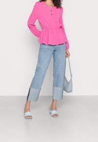 Maglietta rosa a maniche lunghe con vita arricciata, abbinata a jeans azzurri chiari con risvolti e una sottile texture. Sandali con tacco a blocco azzurri chiari.