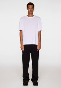 Vit bomulls t-shirt med korta ärmar, avslappnad passform, kombinerad med svarta löst sittande byxor, båda visade mot en neutral bakgrund.