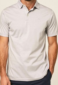 Polo shirt gris clair en tissu lisse avec un col classique, une fermeture à trois boutons et un accent logo subtil. Manches courtes.