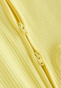 Prim-plan al unui material galben cu dungi, având două cursoruri identice galbene poziționate unul lângă altul pe șina fermoarului.