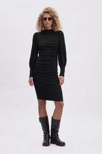 Mustika must dress, millede ripsmete detailidega, pikad puhv-siid-särgid ja kõrge kaelus; koos põlvekõrguste mustade nahkkingadega.