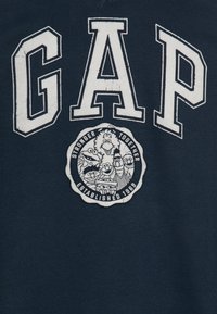 Granatowa bluza z kapturem z dużymi białymi literami "GAP" oraz okrągłą grafiką z postaciami z kreskówek, tekstem "STRONGER TOGETHER ESTABLISHED 1969."