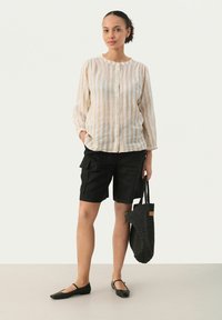 Lightly striped beige and white button-up shirt paired with black cargo shorts and black flats, holding a textured black tote bag.