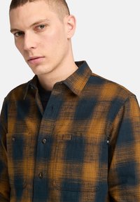 Geruite flanellen shirt in marineblauw en oranje, met een button-down kraag, twee borstzakken en een zachte stofstructuur.