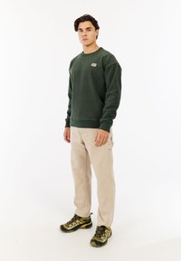 Groene fleecetrui met een gestructureerde afwerking, gecombineerd met beige cargobroeken en donkere sneakers met gele accenten.
