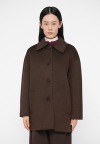 Cappotto marrone in misto lana con collo a risvolto, chiusura frontale con bottoni, due tasche laterali e vestibilità ampia. Tessuto uniforme senza motivi visibili.