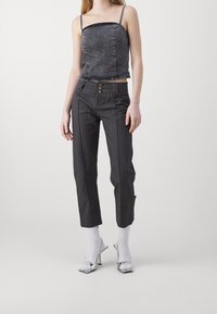 Crop top in denim nero con spalline sottili abbinato a pantaloni a righe nere con tre bottoni e uno spacco laterale, completato da tacchi alti argento.
