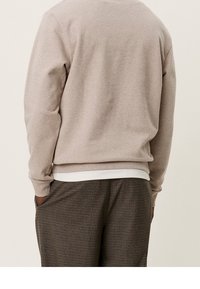 Felpa beige chiaro con scollatura rotonda e polsini a costine, abbinata a pantaloni a quadri marroni con tasche laterali.