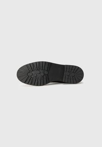 Semelle de chaussure en caoutchouc noir avec une texture nervurée pour une meilleure traction, présentant des motifs circulaires et angulaires, construction solide et durable.
