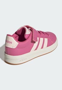 Růžová sportovní obuv s hladkým syntetickým svrškem, třemi bílými pruhy, suchým zipem a bílou gumovou podrážkou.