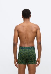 Ανδρικά μπόξερ κατασκευασμένα από ελαστικό βαμβάκι, με πράσινο φυλλώδες σχέδιο, ενισχυμένη ζώνη μέσης σε σκούρο πράσινο με χρυσά γράμματα.