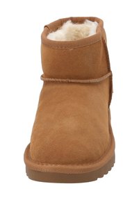 Bota corta de ante color canela con forro de piel suave color crema, punta redonda y suela de goma texturizada. Presenta detalles de costuras a lo largo de las costuras.