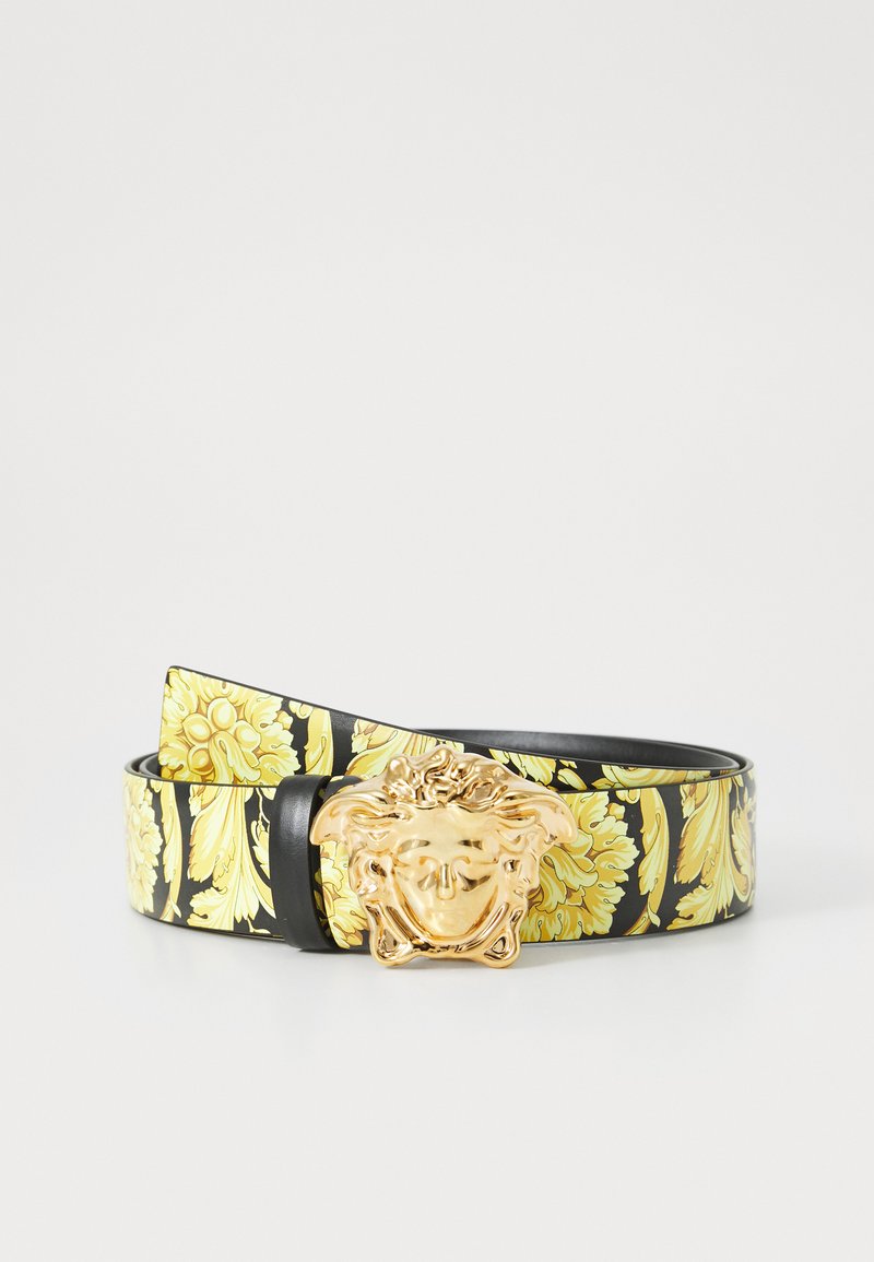 Schwarzer und gelber gemusterter Gürtel mit einer goldenen Medusa-Kopf-Schnalle. Das Material scheint glatt mit einer glänzenden Oberfläche zu sein. Dekoratives Blumendesign vorhanden.