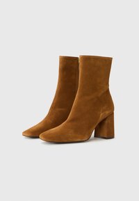 Botas de tobillo de ante marrón con punta afilada y tacón ancho. Cuentan con una cremallera lateral y una textura suave y lisa.