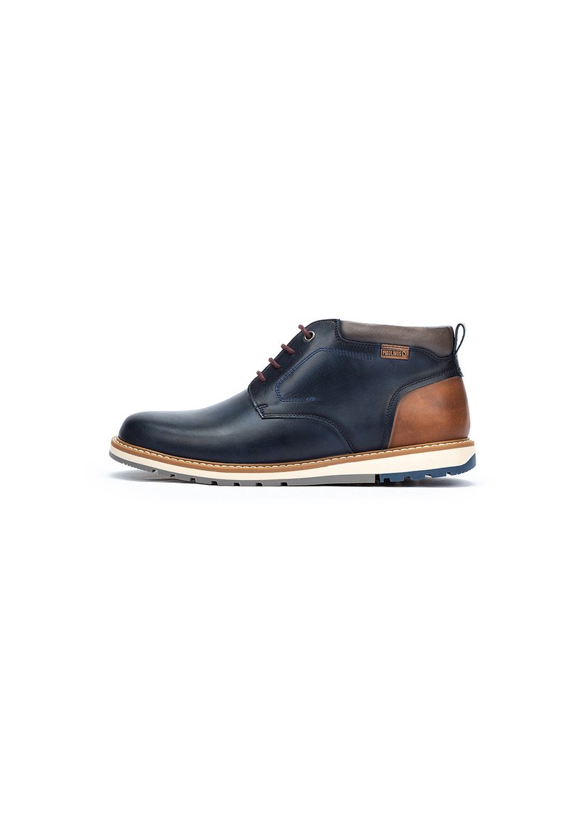 Chukka boot in navy leather with brown accent, featuring a white midsole, six eyelets, and a textured outsole for traction.
