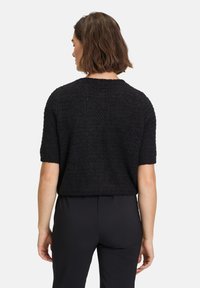 Schwarzer kurzärmeliger Pullover mit strukturierter Strickoptik, im Crewneck-Stil und mit lockerer Passform, kombiniert mit maßgeschneiderten schwarzen Hosen.