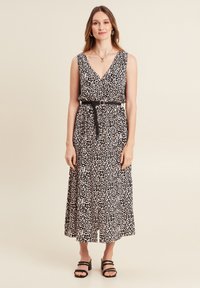 Maxikleid mit Leopardmuster, V-Ausschnitt, ärmellos, mit geraffter Taille und schwarzem Gürtel sowie gestuftem Rock. Flache schwarze Sandalen.