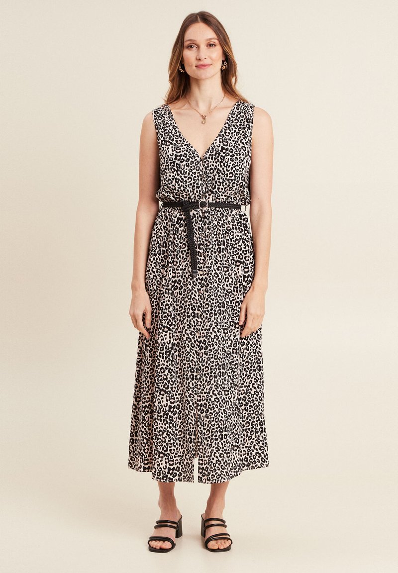 Maxikleid mit Leopardmuster, V-Ausschnitt, ärmellos, mit geraffter Taille und schwarzem Gürtel sowie gestuftem Rock. Flache schwarze Sandalen.