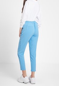 Světle modré slim-fit kalhoty s elastickým pasem a bočními kapsami, spojené s bílou košilí s dlouhým rukávem a bílými teniskami.