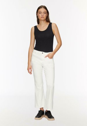 Top nero senza maniche con scollo a barca, abbinato a jeans bianchi a zampa d'elefante e sneaker platform nere; design minimalista e colori neutri.