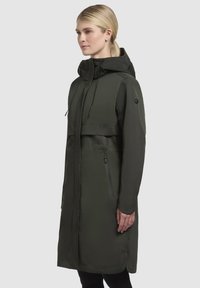 Long dark green waterproof jacket with a hood, zippered pockets, and a sleek design. Smooth texture with a modern silhouette.