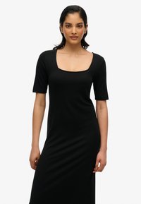 Robe noire cintrée avec des manches courtes, décolleté carré et texture lisse. Le tissu est extensible, permettant un look ajusté.