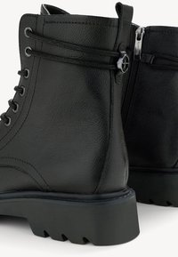 Čierne kožené členkové čižmy s kovovými očkami, šnurovaním, textúrovaným zvrškom a bočným zipsom. Obsahujú robustnú, vzorovanú gumovú podrážku.