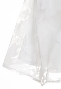 Vit genomskinlig tyg med stort blommigt jacquardmönster och scalloped kant, mjukt flödande och något genomskinligt.