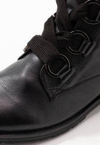 Botte en cuir noir avec une finition texturée, dotée de passants en métal ronds, de lacets noirs épais et d'une semelle en caoutchouc.