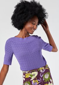 Light purple knit sweater with short sleeves featuring textured, wavy pattern, paired with floral print, purple, and green skirt.