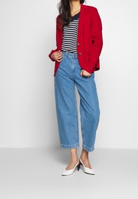 Červený blejzr, námořnicko-modré a bílé pruhované tričko, světle modré široké džíny s vysokým pasem a bílé boty na vysokém podpatku.