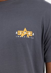 Hallide hallist puuvillane t-särk lühikeste varrukatega, mille vasakul rinnal on kollane ja valge trükitud logo kujundus.