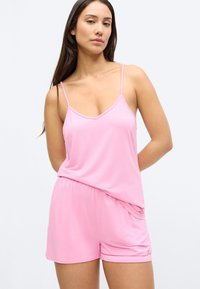 Roosa pidžaamakomplekt, mis on valmistatud kergest ja pehmest kangast. Ülaosas on õhukesed rihmad ja V-kaelus; lühikesed püksid koos elastse vöökohaga.