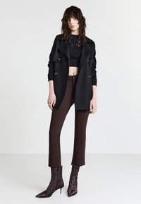 Manteau noir à double boutonnage, top noir court, pantalon évasé marron et bottines à talons aiguilles en imprimé léopard.
