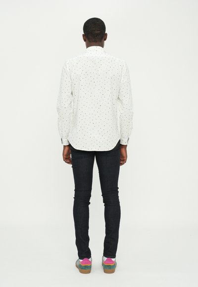 White button-up shirt with multicolored dot pattern, long sleeves and rounded hem, paired with dark denim jeans and multicolored shoes.