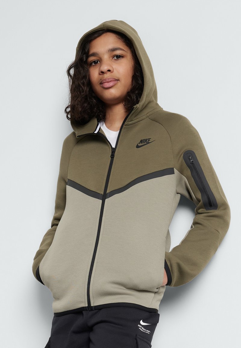 Felpa con zip Nike in verde oliva e beige. Presenta un cappuccio, accenti neri in contrasto, tasche laterali e una piccola tasca con zip sulla manica.