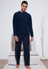 Mornarska majica s dugim rukavima za pidžamu s kare uzorkom na džepu, u kombinaciji s pidžama hlačama u kare uzorku u mornarskoj plavoj i bijeloj boji, s opuštenim krojem.