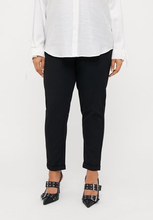 Person wearing black slim-fit pants with rolled cuffs, a white buttoned shirt with tied cuffs, and black pointed heels with double buckle straps.